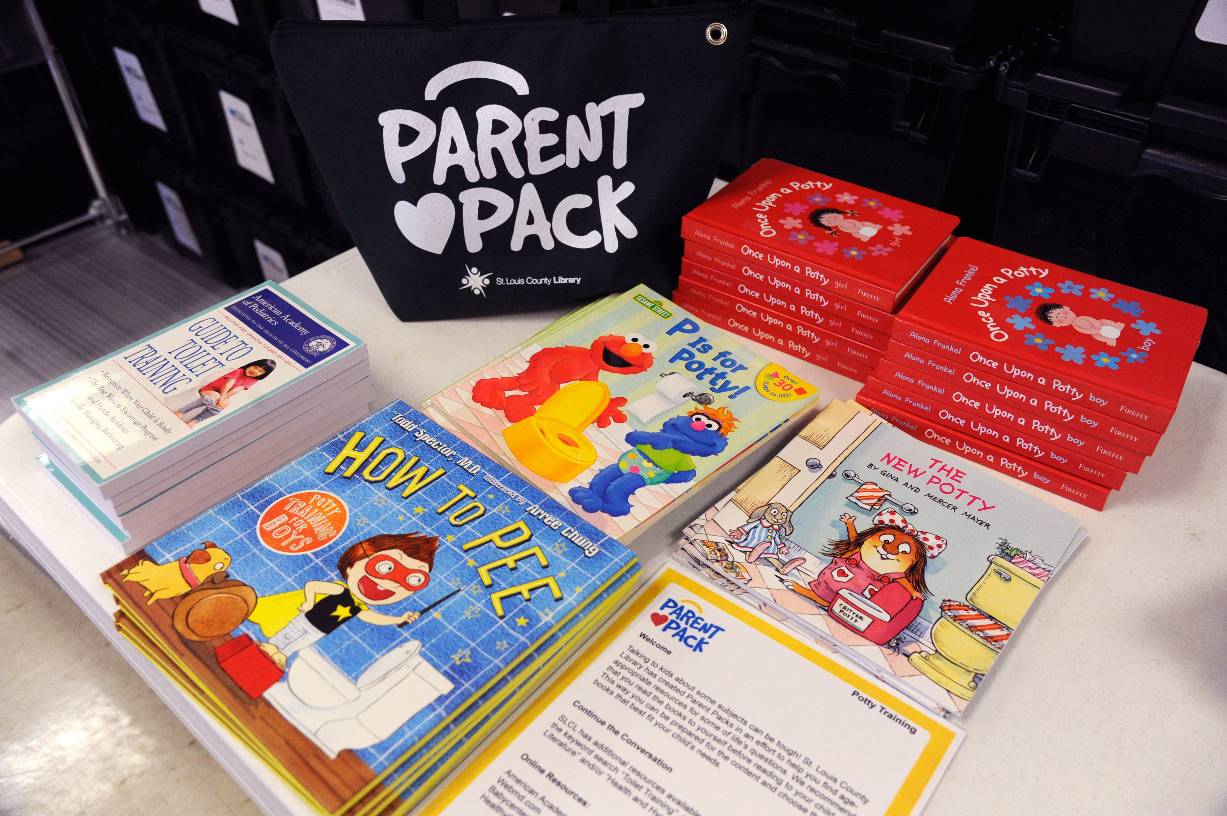 Dark blue bag with Parent Pack and a heart printed in white on it with books on potty training stacked on a table