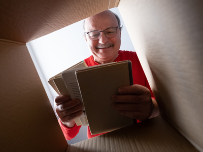 A camera view looking up inside a cardboard box finds an older man with glasses pulling books out