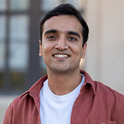Jitesh Jaggi smiling and wearing a white shirt with a dark red button down shirt over it